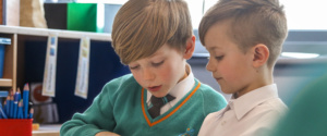 Two pupils are seen sat at a desk reading together.