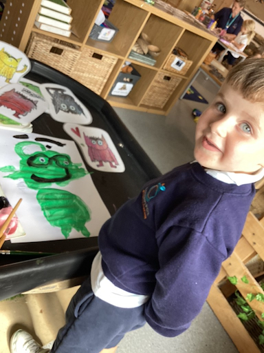 A young boy from Nursery is pictured smiling for the camera, after having painted some pictures of characters.