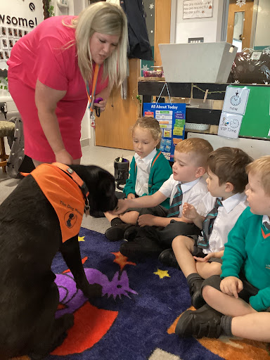 A photo showing a member of staff and a small group of pupils petting Willow the Dog Mentor in a classroom.