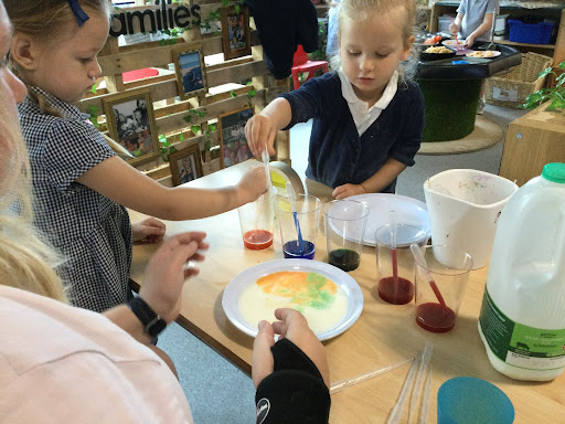 Two young female pupils are pictured stood at their desks, participating in an Arts & Crafts class and mixing different paint colours together.