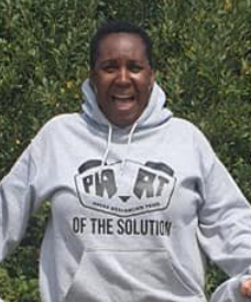 A woman is pictured smiling for the camera outdoors, whilst wearing a grey Panda Anti-Racism Team hoodie.